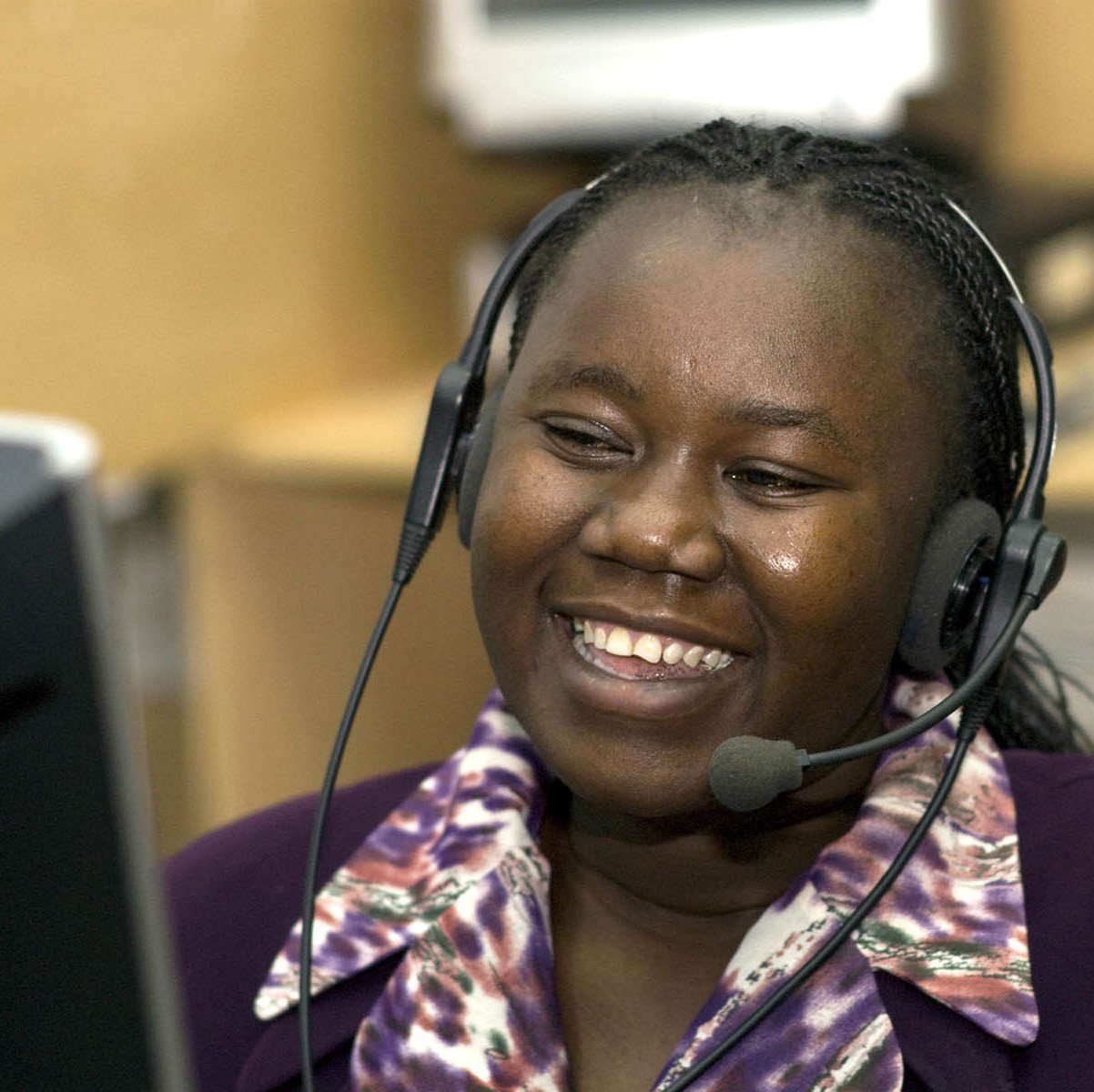 Young black woman with headphones smiling at her computer screen